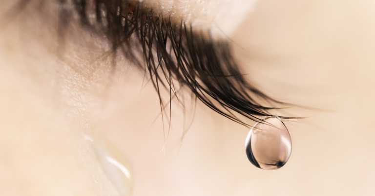 Sad woman concept – closed eyelid closeup with a teardrop on eye