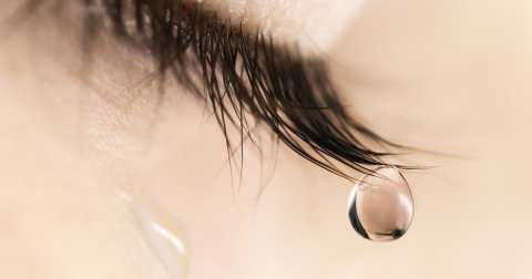 Sad woman concept – closed eyelid closeup with a teardrop on eye