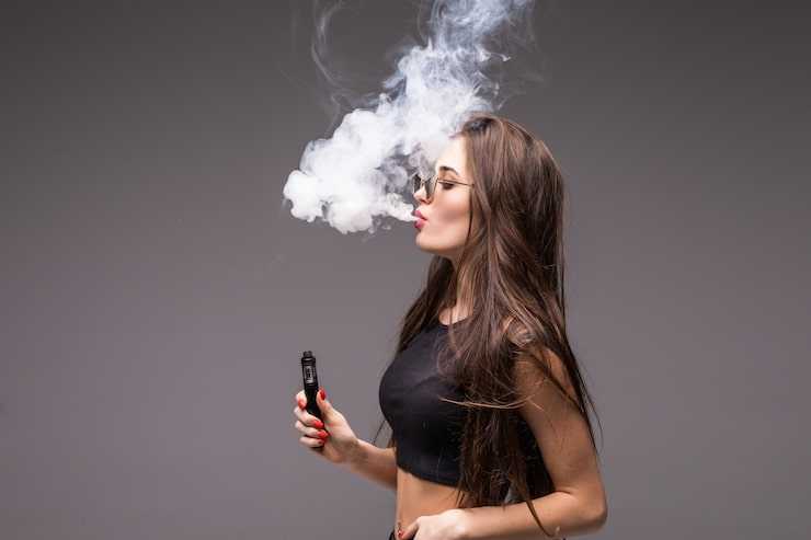 young-woman-sunglasses-black-clothes-vaping-blowing-smoke-electronic-cigarette-gray-wall_231208-3713