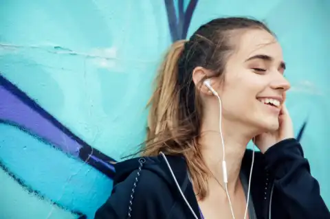 Smiling,Young,Woman,With,Smartphone,And,Headphones,Listening,To,Music