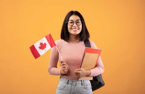 travel-modern-education-and-student-exchange-young-cheerful-asian-woman-in-glasses-with-notebooks-backpack-holding-small-flag-of-canada-isolated-on-beige-background-studio-shot-empty-space-photo